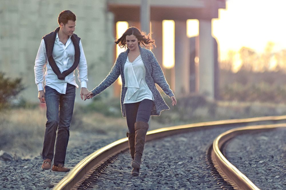 Couple walking playfully along railroad tracks during engagement photoshoot.