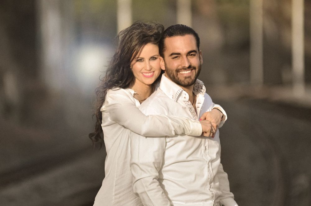 Couple wearing white and dark outfits poses intimately in outdoor setting.