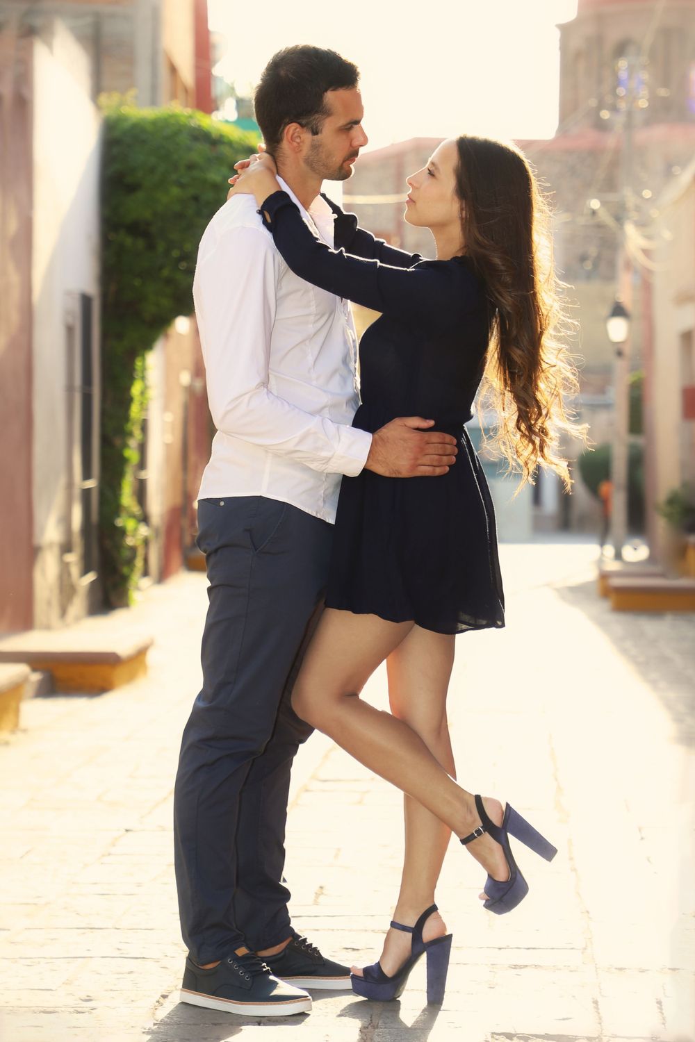 Dancing couple in elegant outfits twirls through sunlit street.