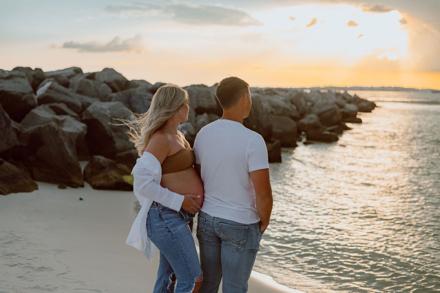 Couple walking hand in hand through beach dunes at sunset.