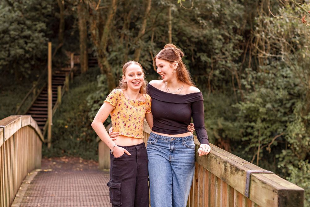 Two people in casual attire walk together and laugh on a wooden bridge surrounded by lush greenery. Bledisloe Park, Palmerston North