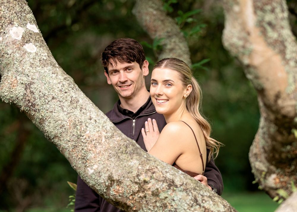 A couple shares a romantic moment together while sitting in a tree in a natural outdoor setting.
