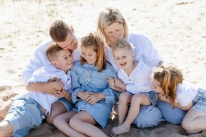 A family in white and blue outfits sits together on a sandy beach for a casual photo session.