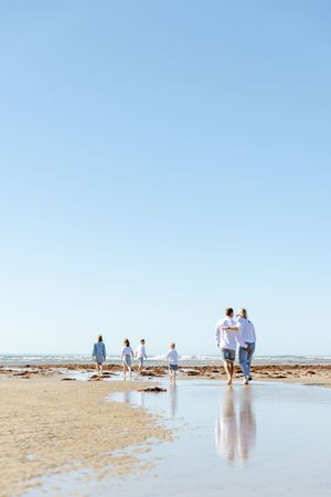 Silhouettes of people walking along a serene beach shoreline with reflections in the wet sand during low tide.