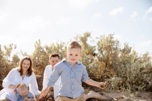 little boy running towards the camera with their family cuddling and laughing behind them on the beach in Portarlington
