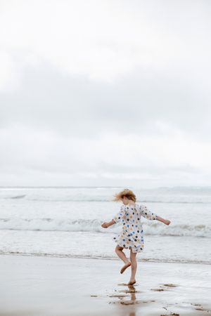 Young girl spinning around near the water on the beach in Ocean Grove