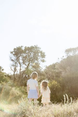 Two people sit together in a sunlit meadow with tall grass and trees silhouetted against a golden afternoon sky.