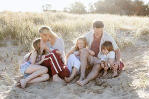 A family sits together on a sandy beach path during golden hour sunset creating a warm and intimate outdoor portrait.