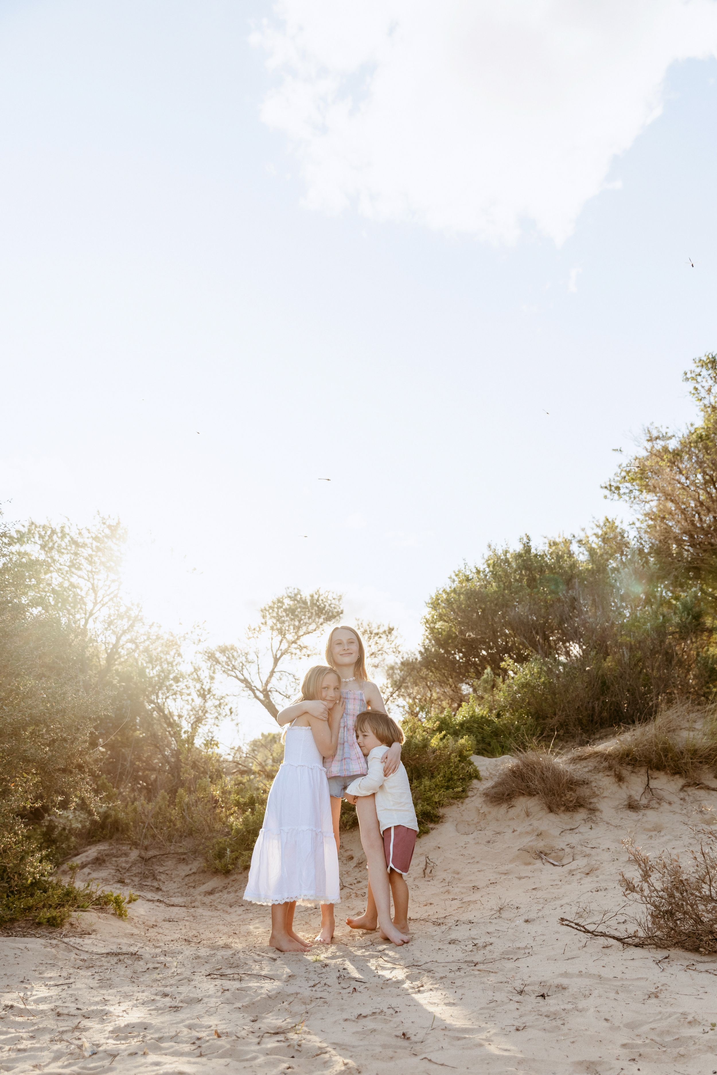 Family in white outfits embracing on sandy beach dunes during golden hour sunset.