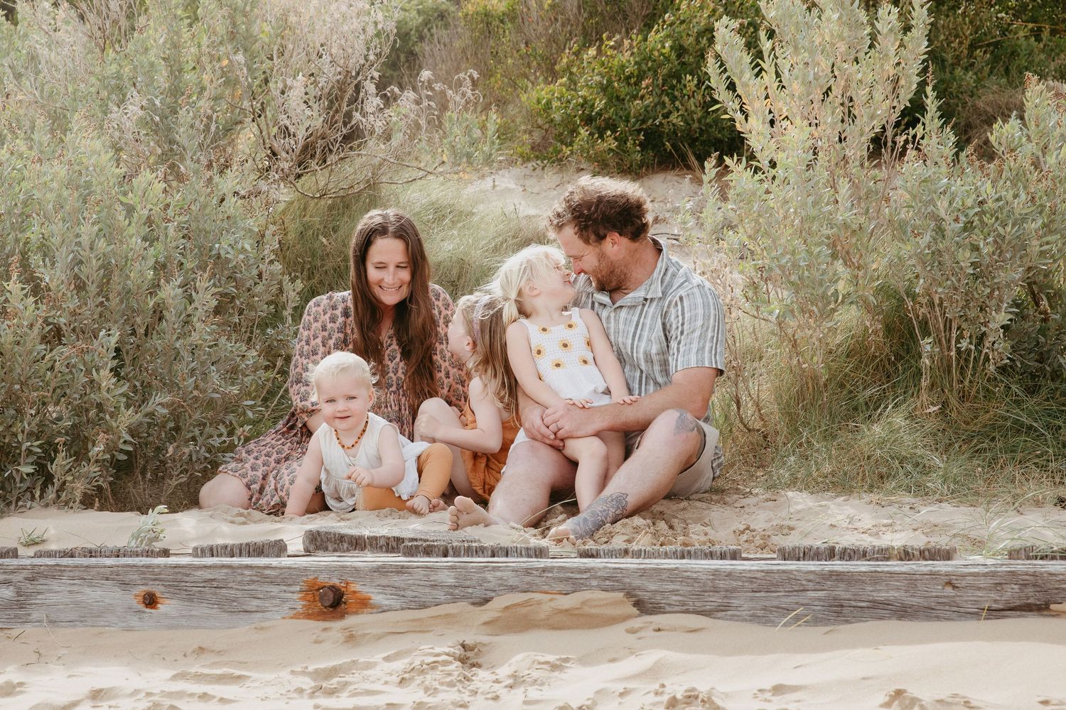 Family sitting and laughing on the beach with the sand dunes behind them, Ocean Grove, Victoria