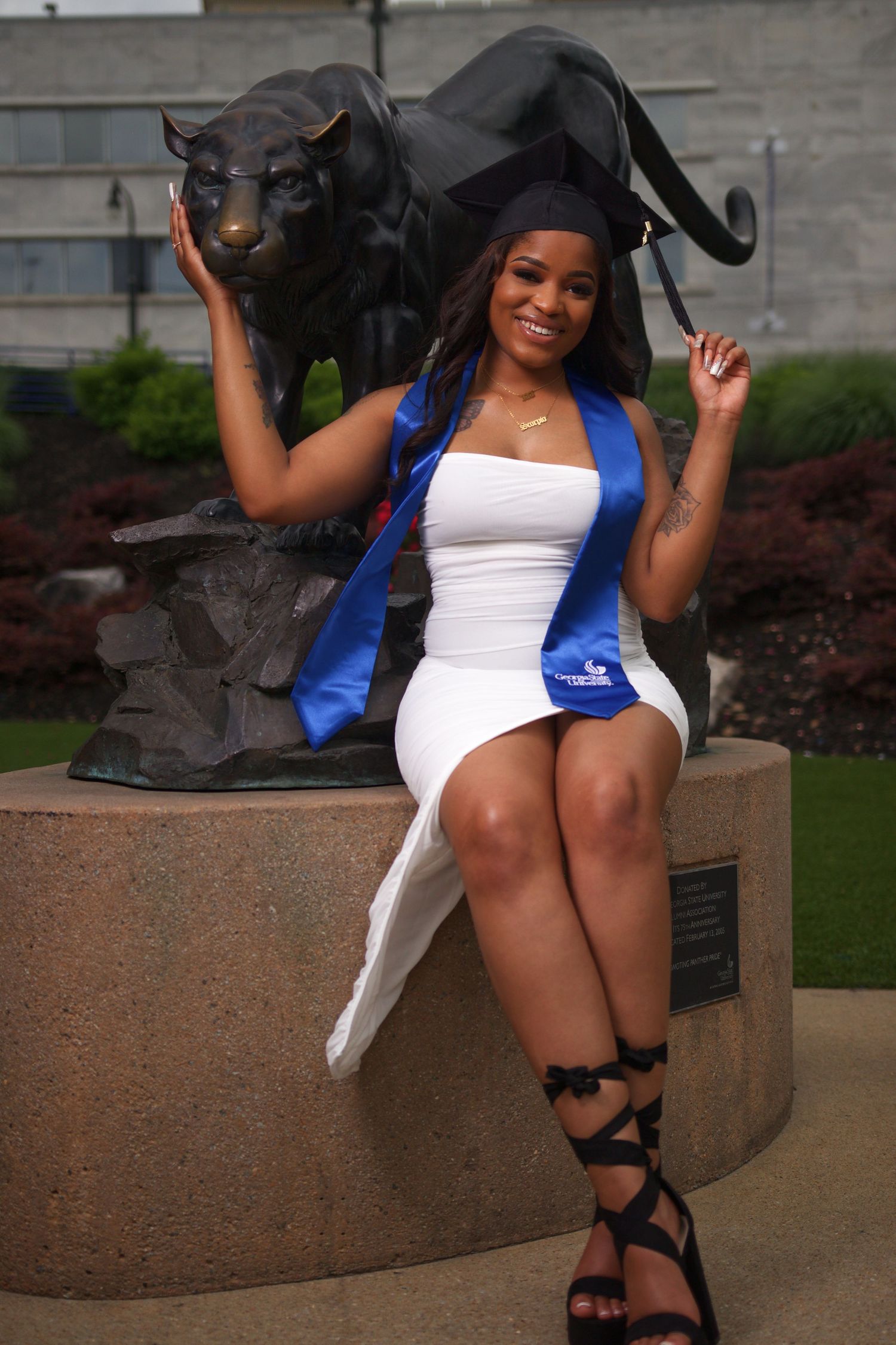Graduate posing in cap and gown beside the Panther statue outside the Student Center at Georgia State University