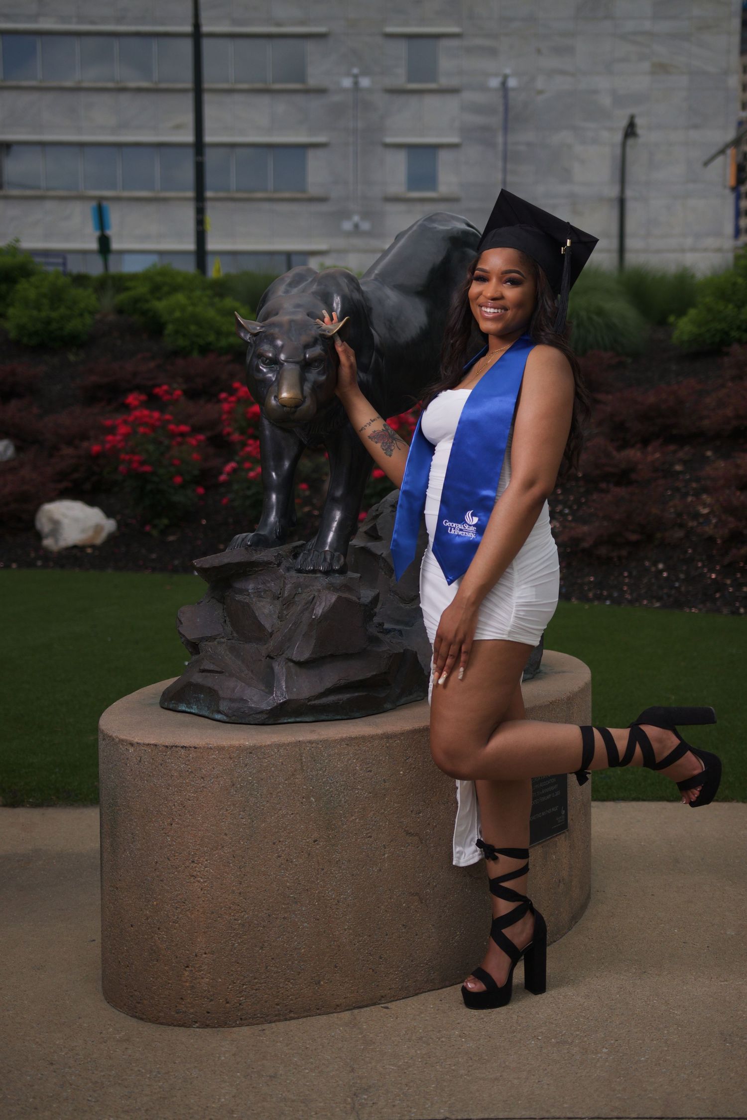 Graduate posing in cap and gown beside the Panther statue outside the Student Center at Georgia State University