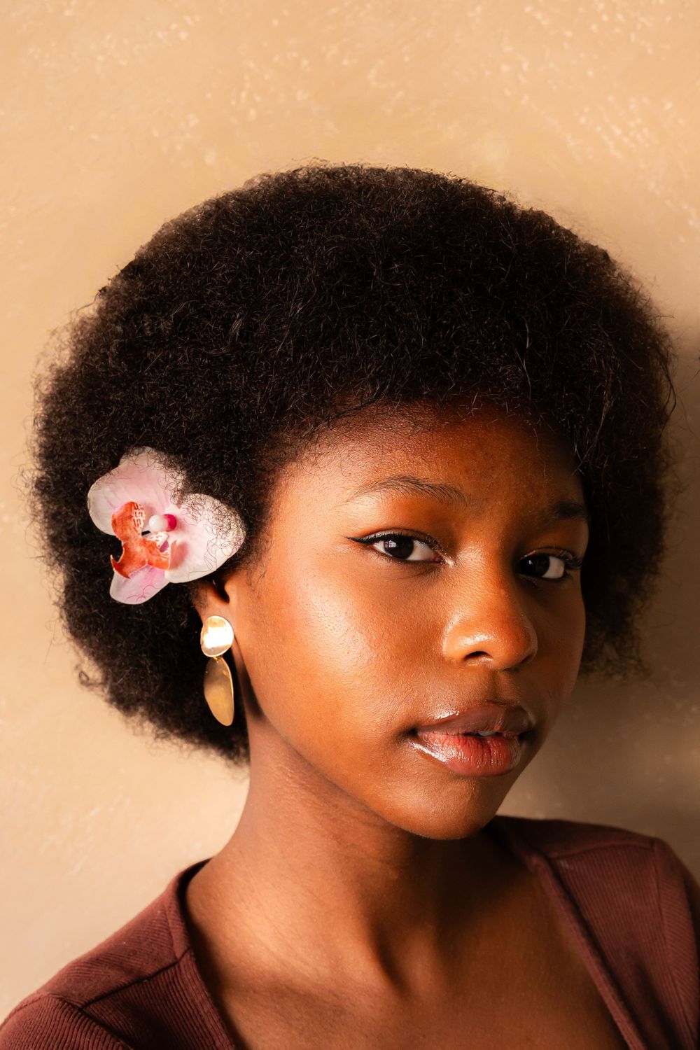 Beauty portrait featuring natural afro hairstyle adorned with pink orchid flower against peachy backdrop.