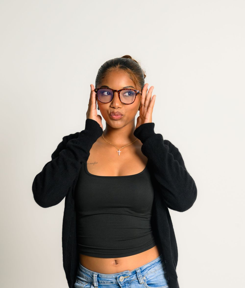 Casual portrait in black crop top and denim with hands framing glasses.