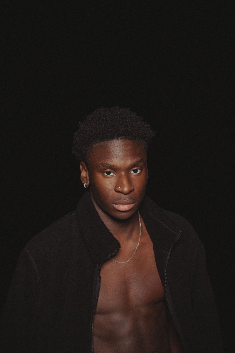 Dramatic low-light portrait of muscular torso in open black jacket.