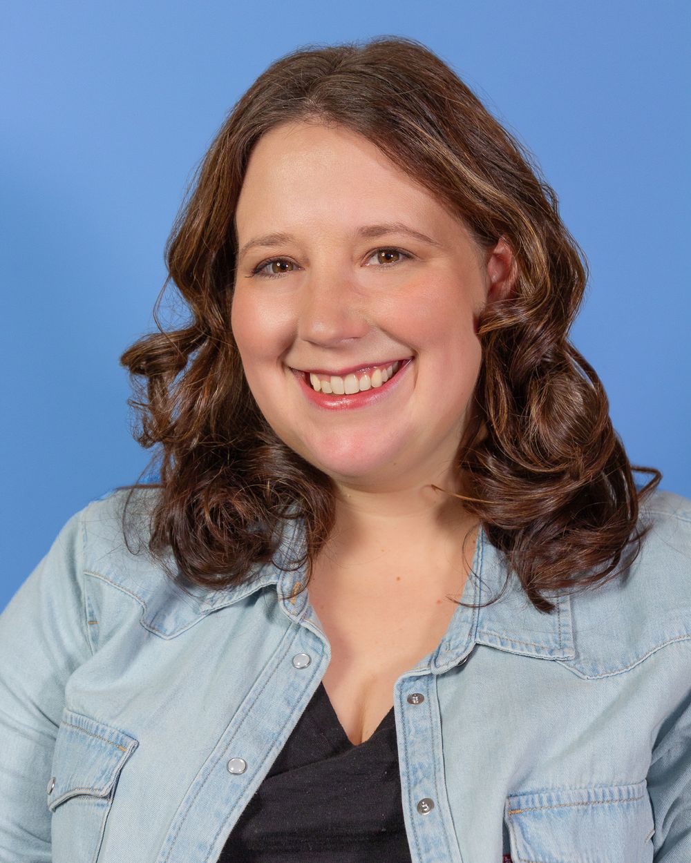 Professional portrait in denim shirt against blue background.