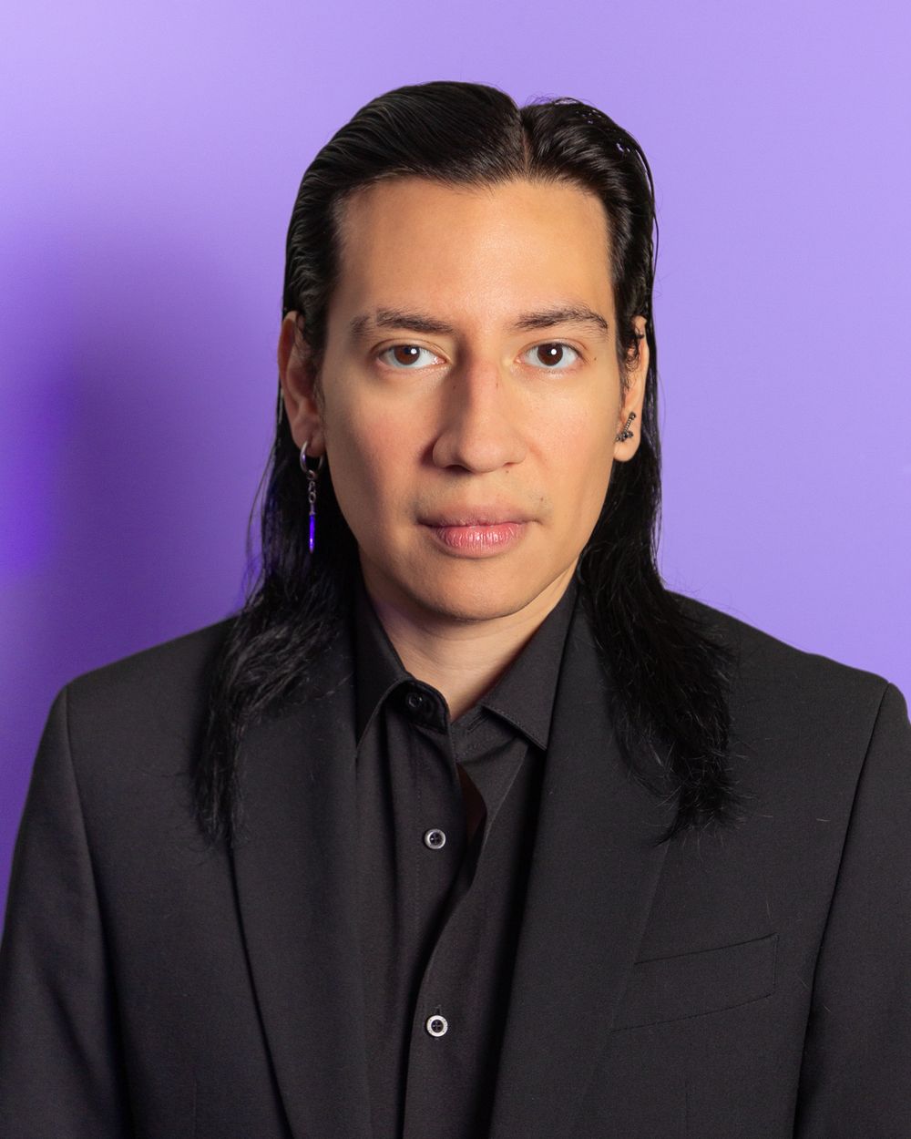 Professional headshot against purple background wearing black suit and shirt.