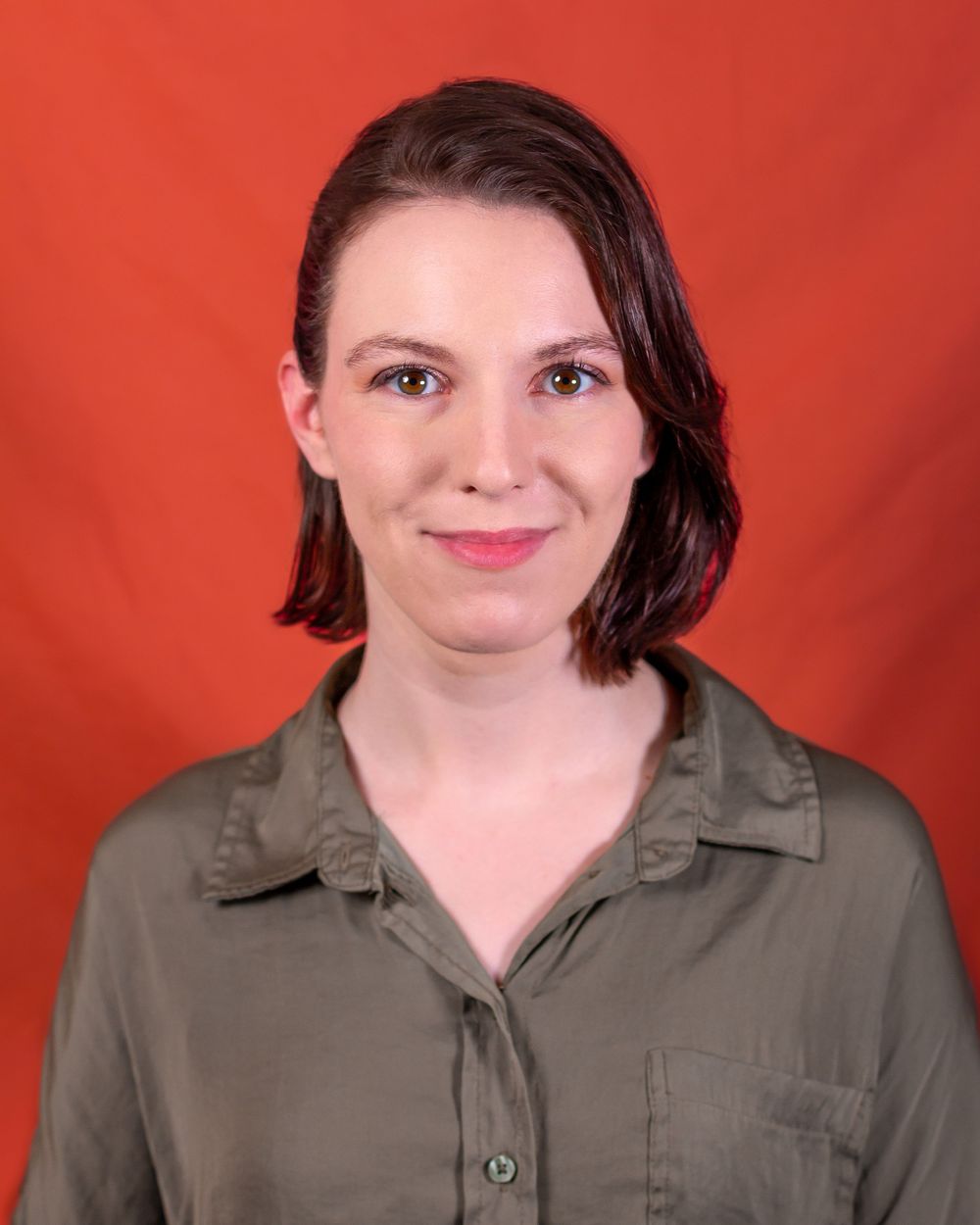 Portrait of someone wearing an olive button-down shirt against an orange background.