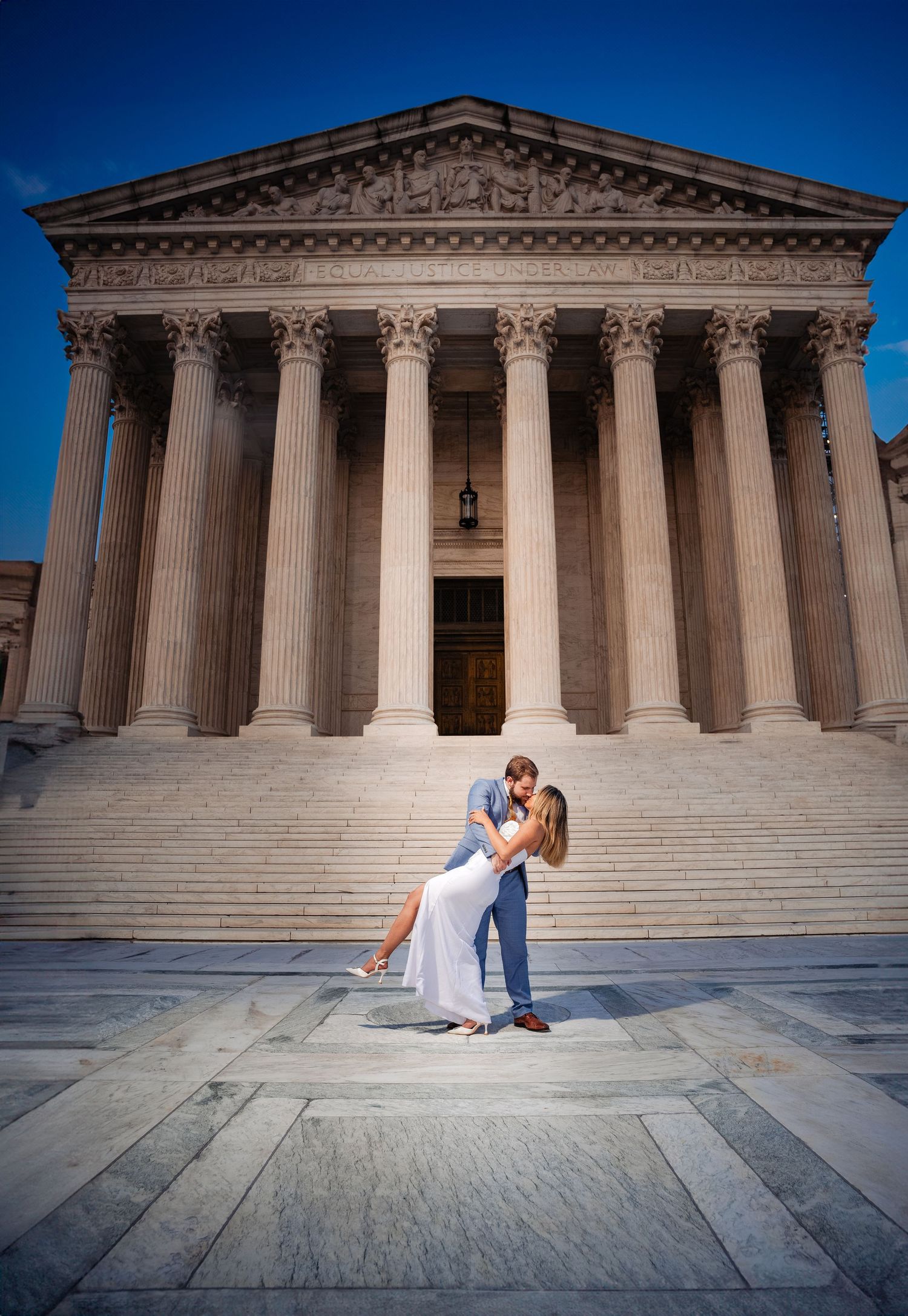 Romantic couple in elegant attire shares a dramatic dip pose in front US Supreme Court with towering columns and steps.