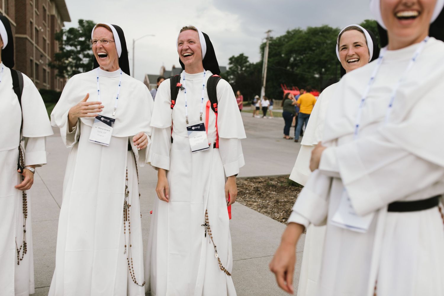 Group of nuns in white habits sharing a lighthearted moment outdoors.