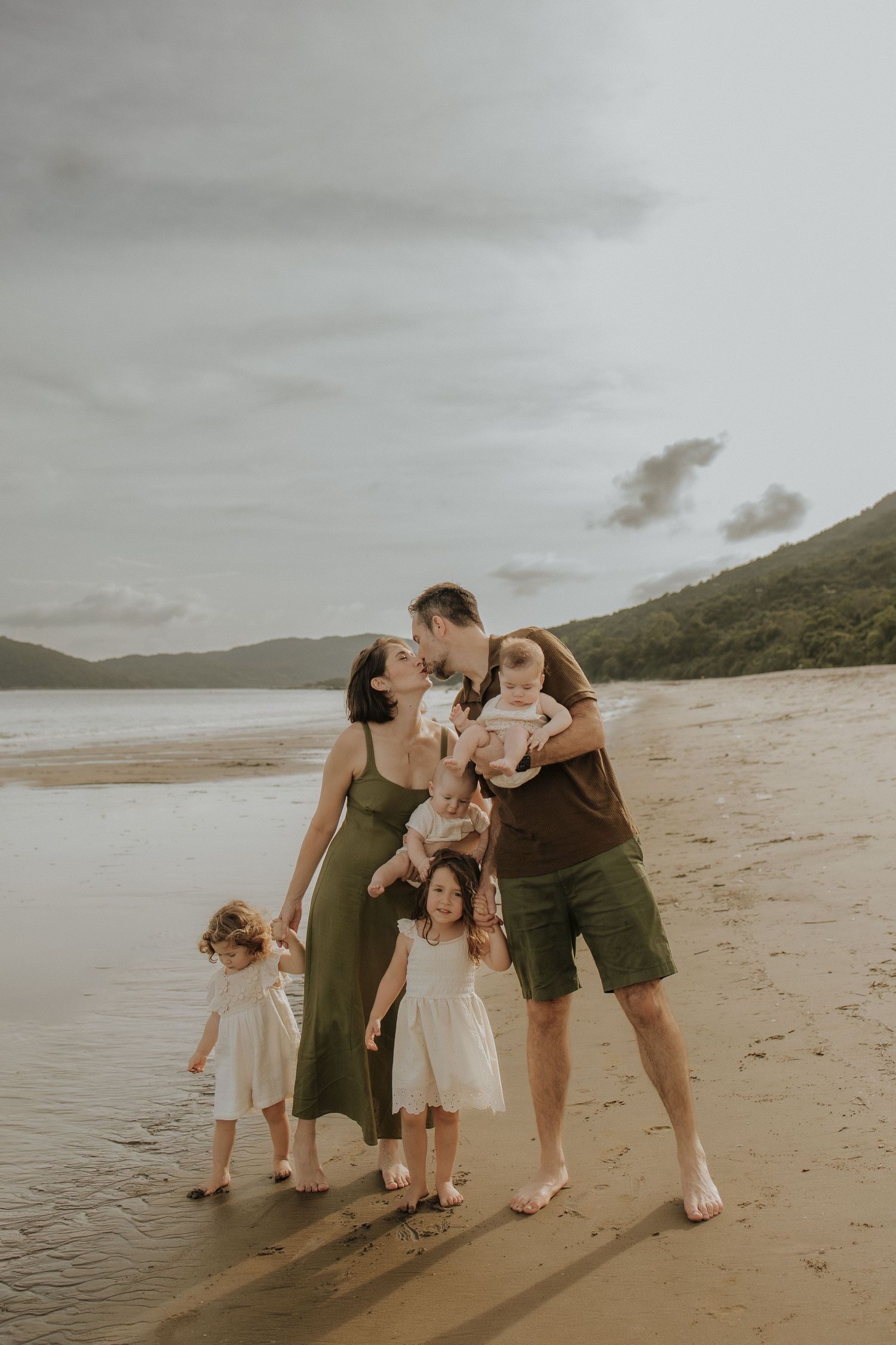 A family shares an intimate moment together on a scenic beach at sunset with mountains in the background.