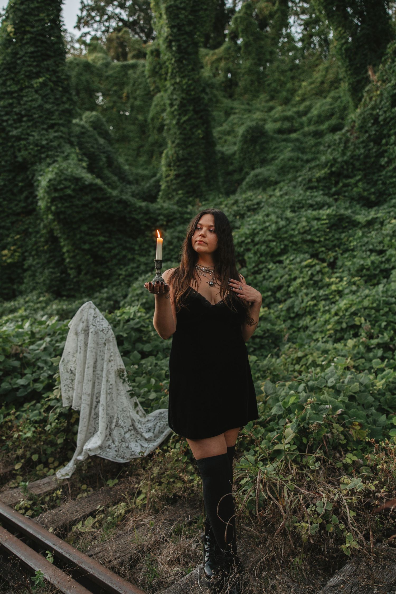 Artistic outdoor photoshoot in a lush green forest setting showing dynamic movement and flowing black clothing.