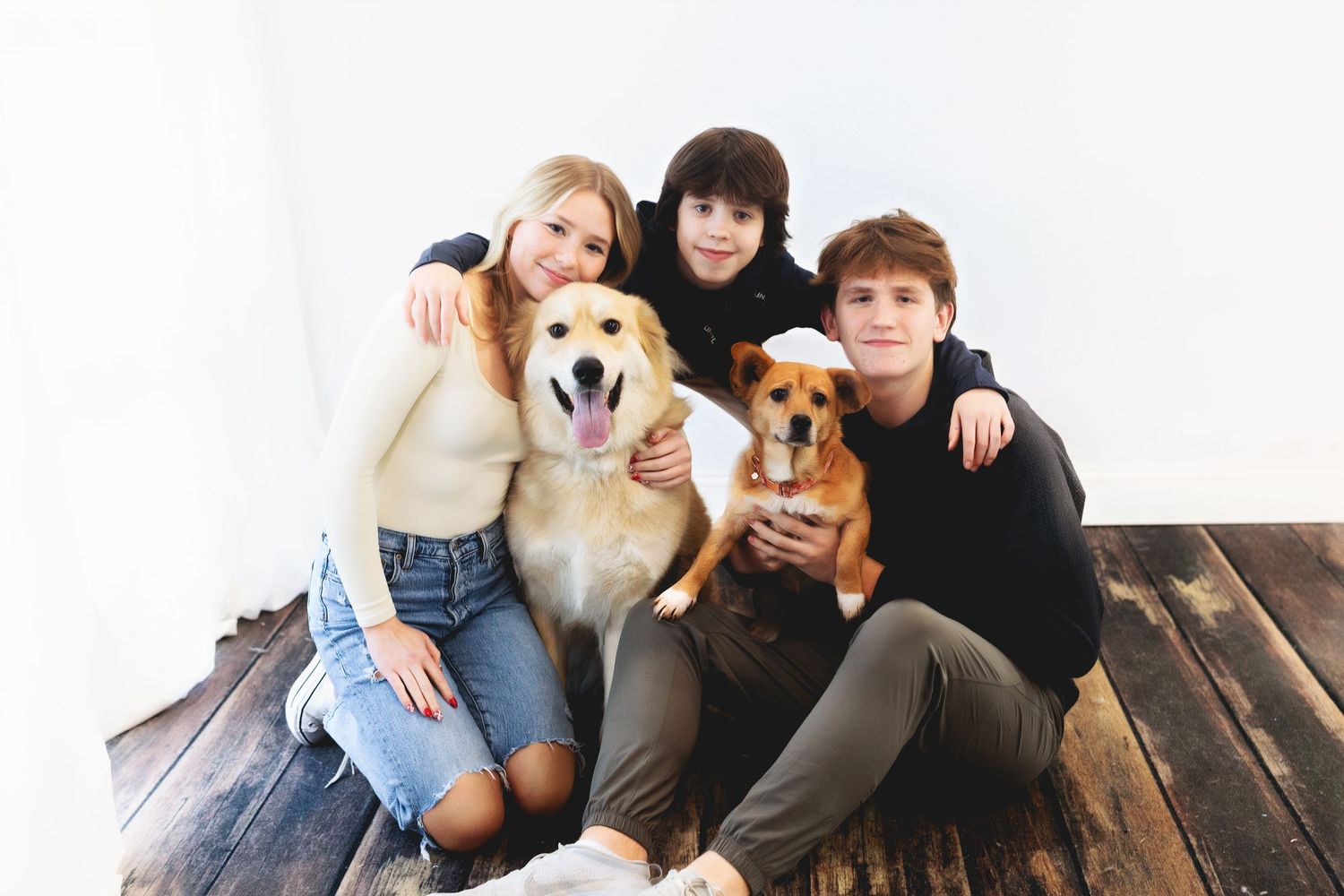 Group photo with two golden retrievers and their owners sitting on wooden floor.