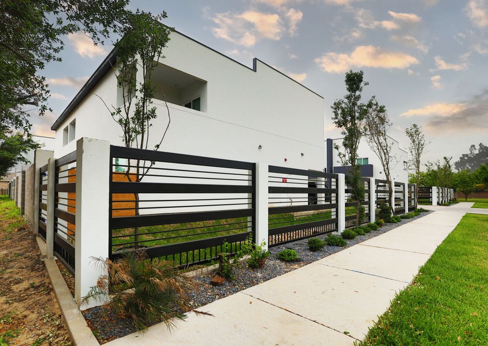 Modern white house exterior with black horizontal fence and landscaped pathway.