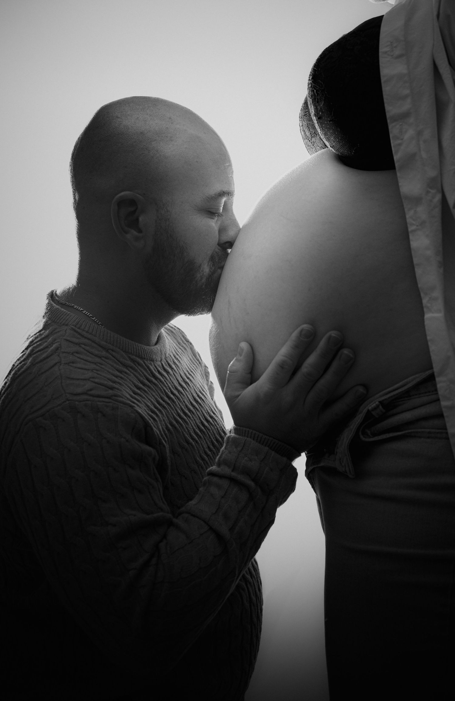 Papa embrassant le ventre de la maman enceinte en noir et blanc lors d’un photoshoot de maternité à Ange-Gardiens, Québec.