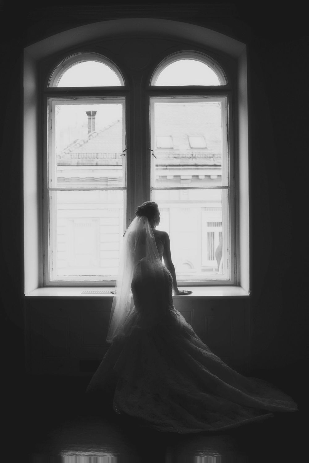 Silhouette of bride in flowing dress gazing through arched window.