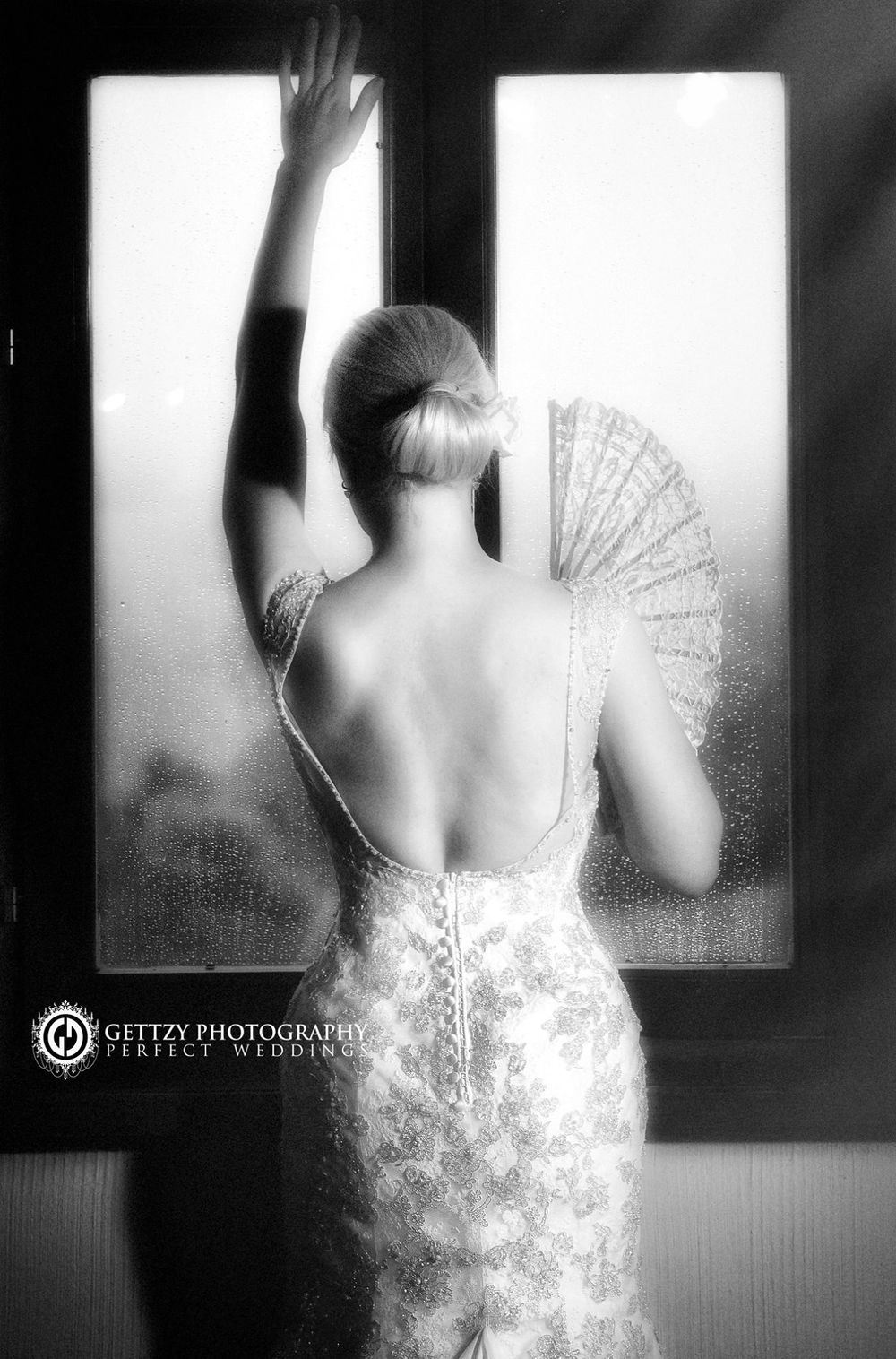 Artistic black and white silhouette of bride in lace dress holding decorative fan.