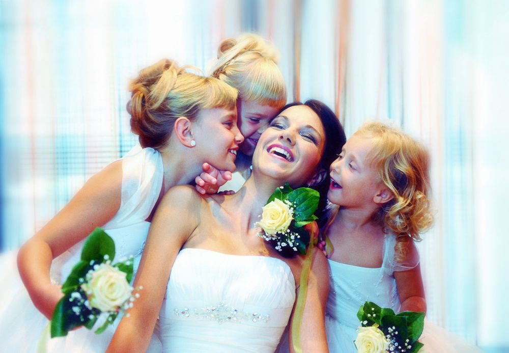 Three women laughing joyfully together at wedding celebration with flower corsages.