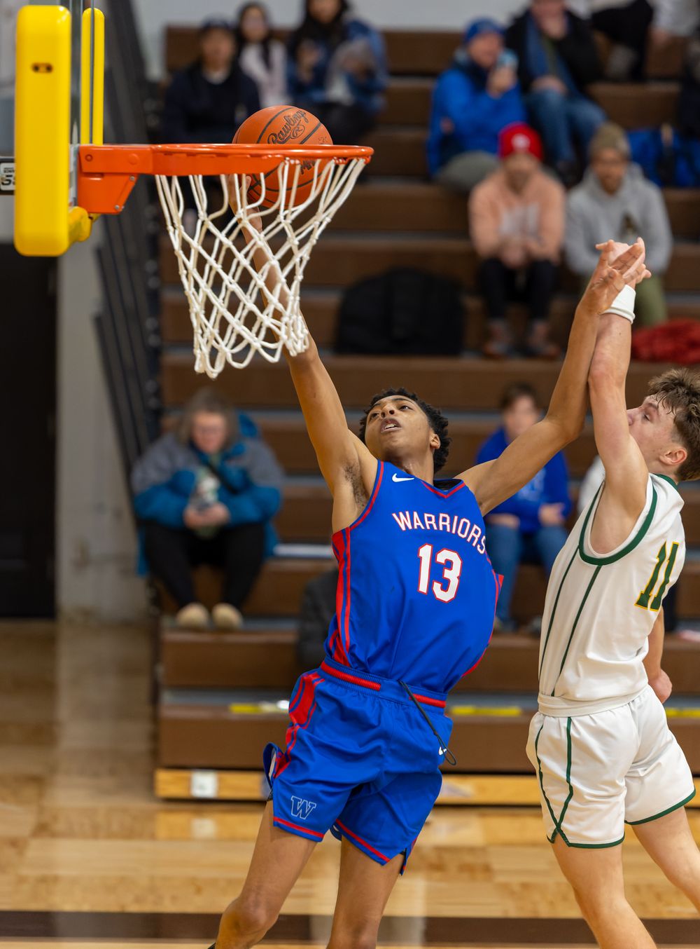 Two basketball players leap high to compete for a rebound during an intense game on the hardwood court.
