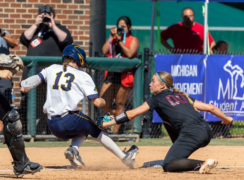 Softball player #13 slides into home plate as catcher attempts tag during competitive college game.