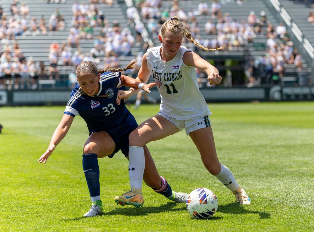 Two female soccer players compete for the ball during a college match on a green field.