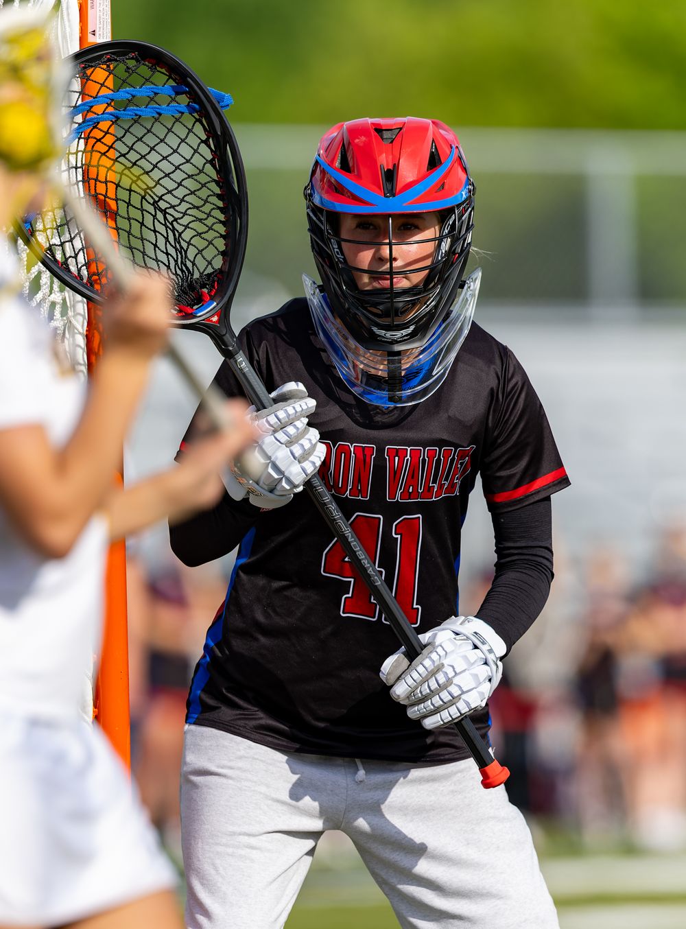 Lacrosse goalie wearing #41 jersey and red helmet guards the net during a competitive match.