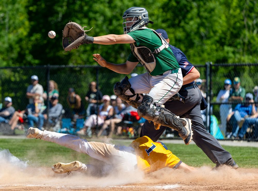Baseball catcher reaches for ball as runner slides into home plate in a dusty youth baseball game.