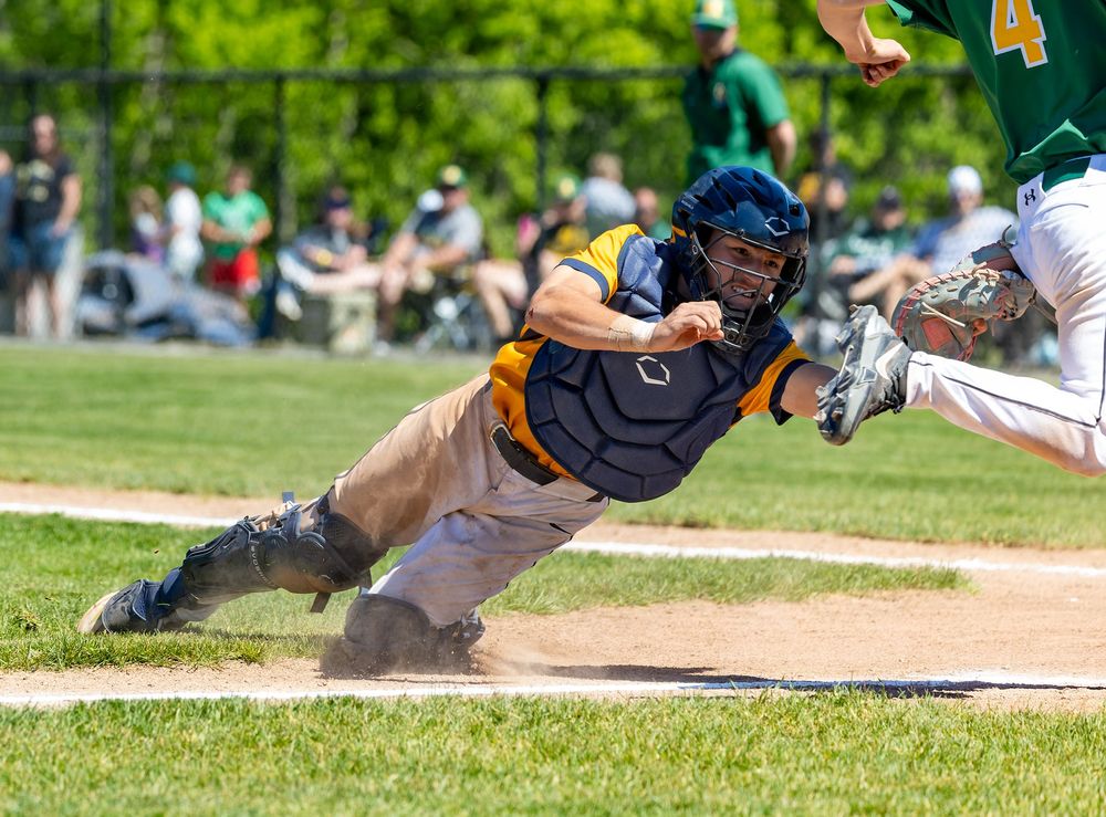 Baseball catcher diving to tag out a runner sliding into home plate during a sunny outdoor game.
