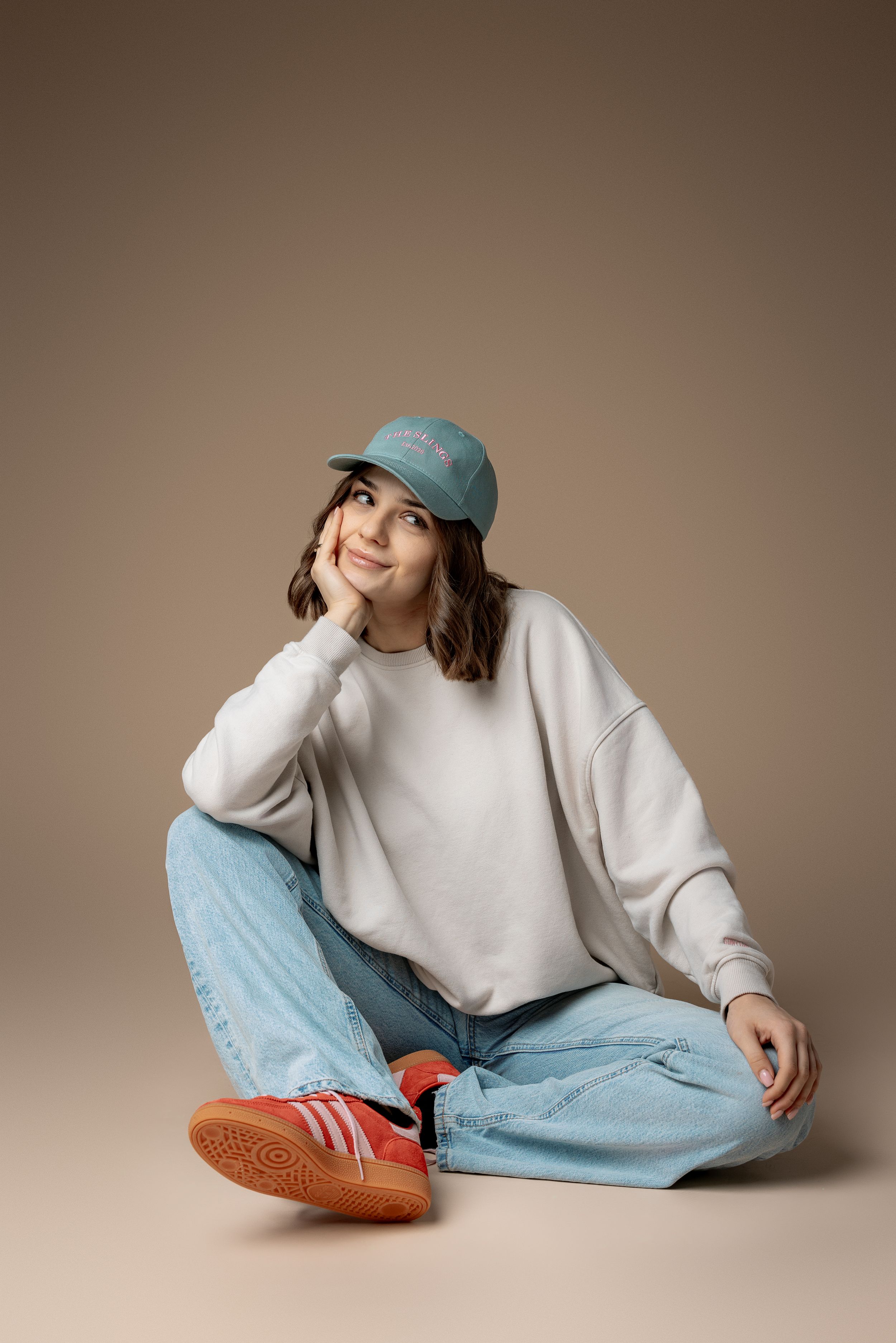 Casual outfit with white sweater, light blue baseball cap, and jeans against neutral backdrop.