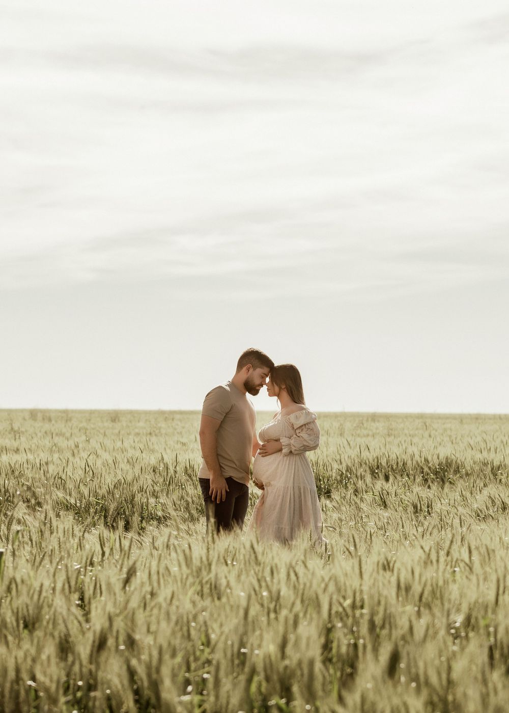Romantic couple embraces in a golden wheat field at sunset creating a dreamy countryside silhouette.