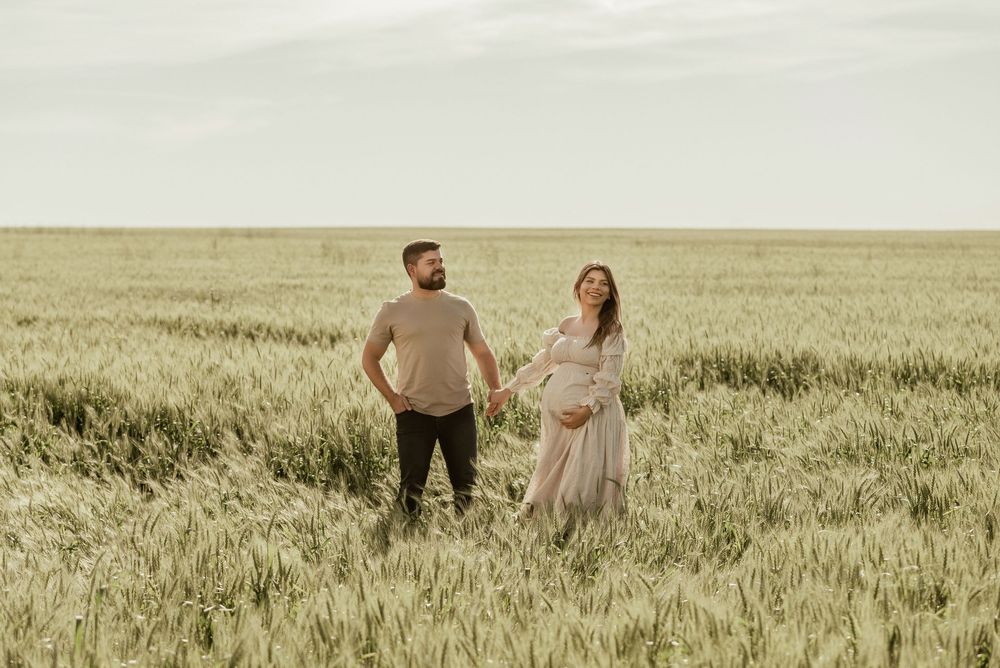 A couple walks through a golden wheat field at sunset holding hands and enjoying the serene countryside view.