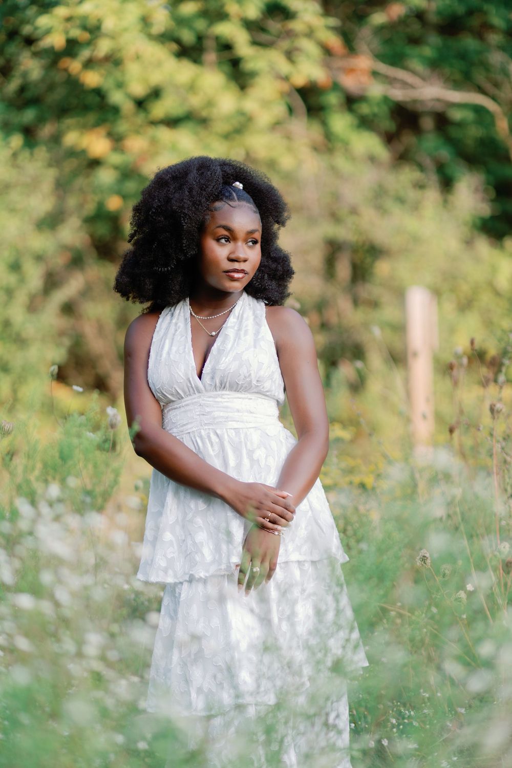 Portrait of a woman wearing a white tiered dress posing in a dreamy outdoor garden setting.