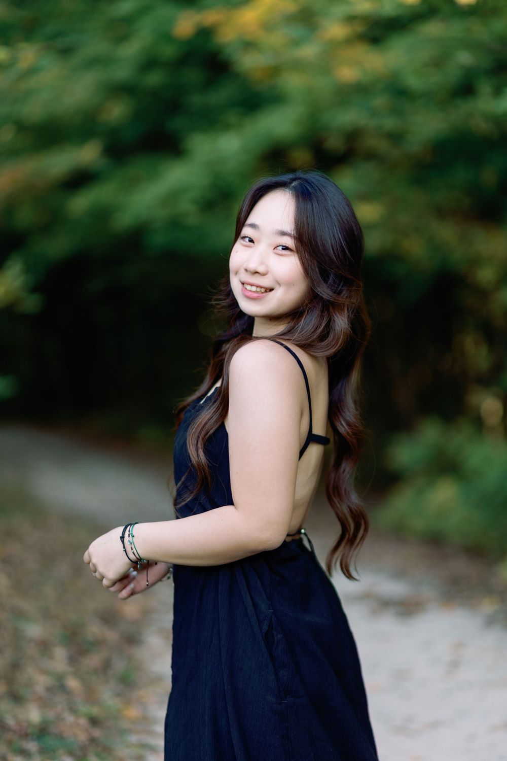 Portrait of someone in a navy blue sleeveless dress standing on a path with green foliage in the background.