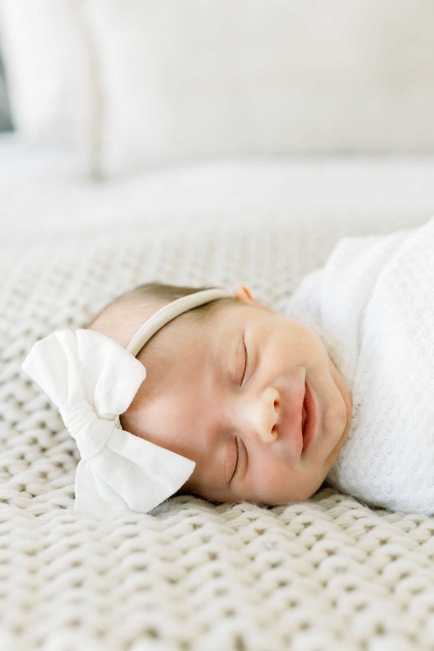 Close-up of sleeping newborn with white bow headband on knitted blanket.