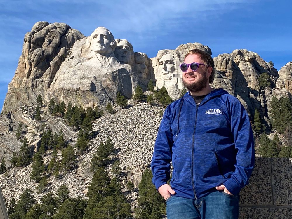 Tourist posing in front of Mount Rushmore on clear sunny day.