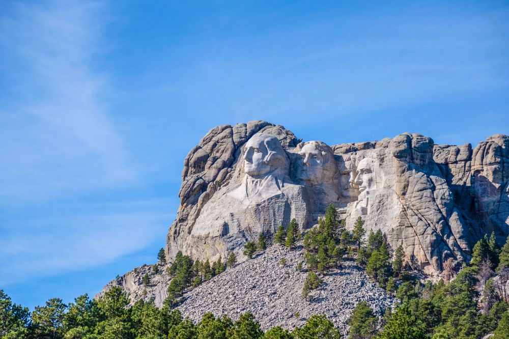 Mount Rushmore monument carved into granite rock face against bright blue sky.