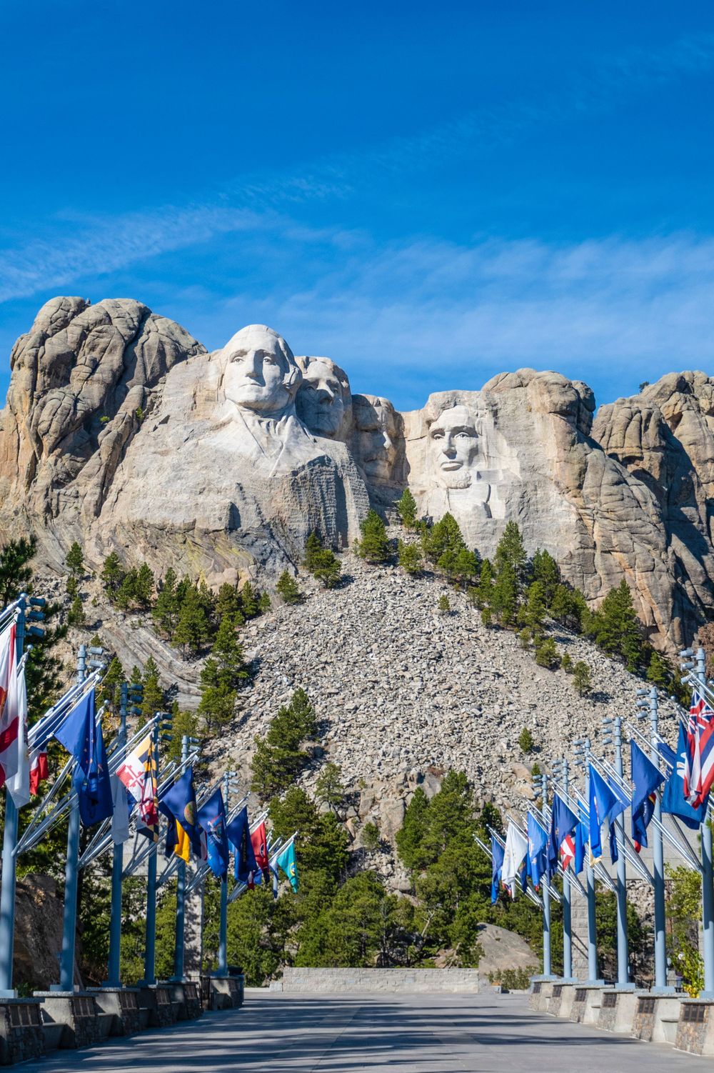 Mount Rushmore National Memorial viewed through an avenue of American flags on a sunny day.