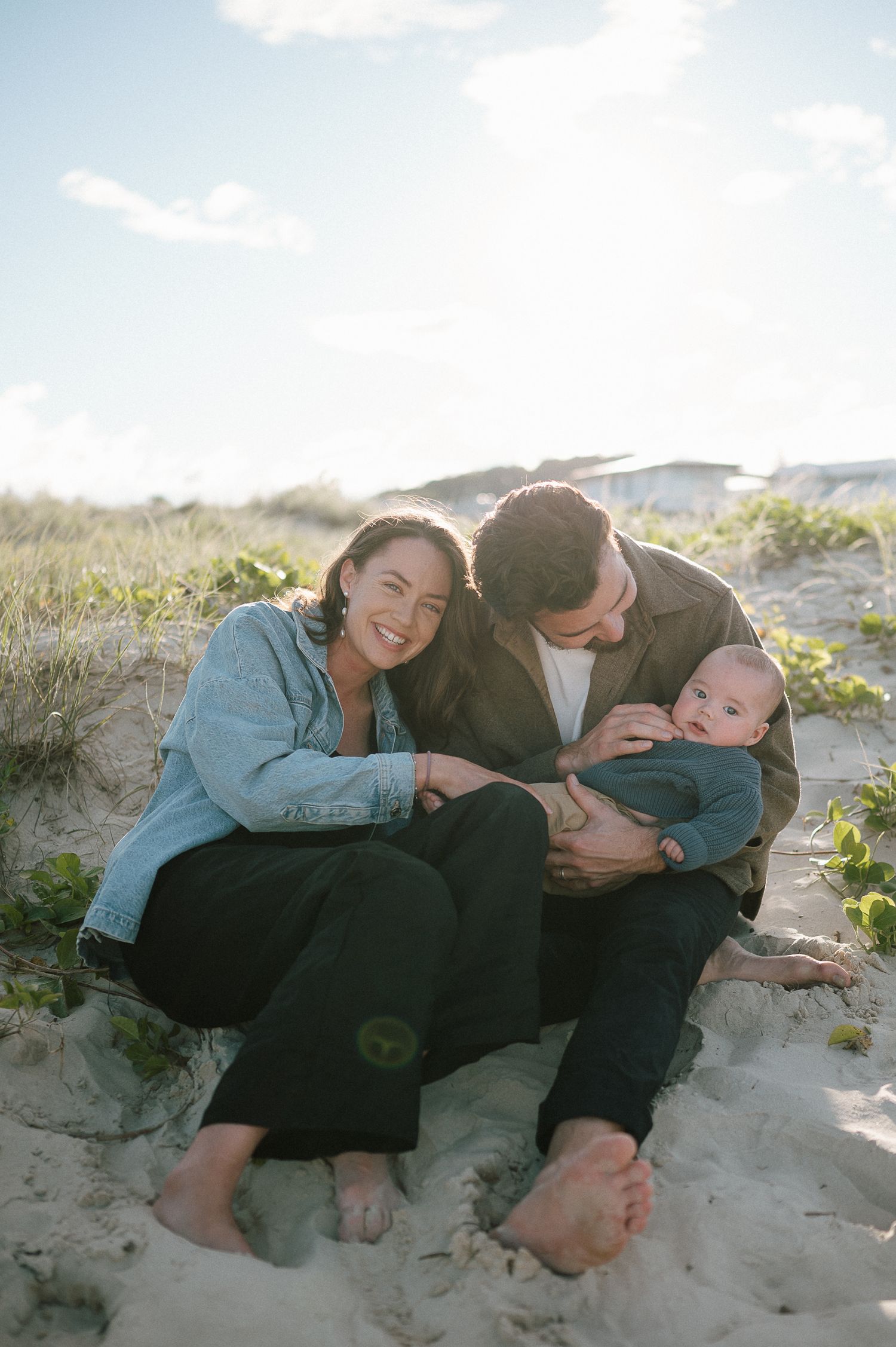 Family relaxing together on sandy beach dunes on a sunny day.
