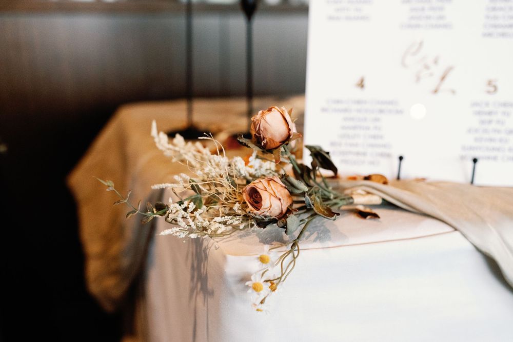 Dried floral arrangement with roses and wildflowers beside a seating chart at an elegant wedding reception table.