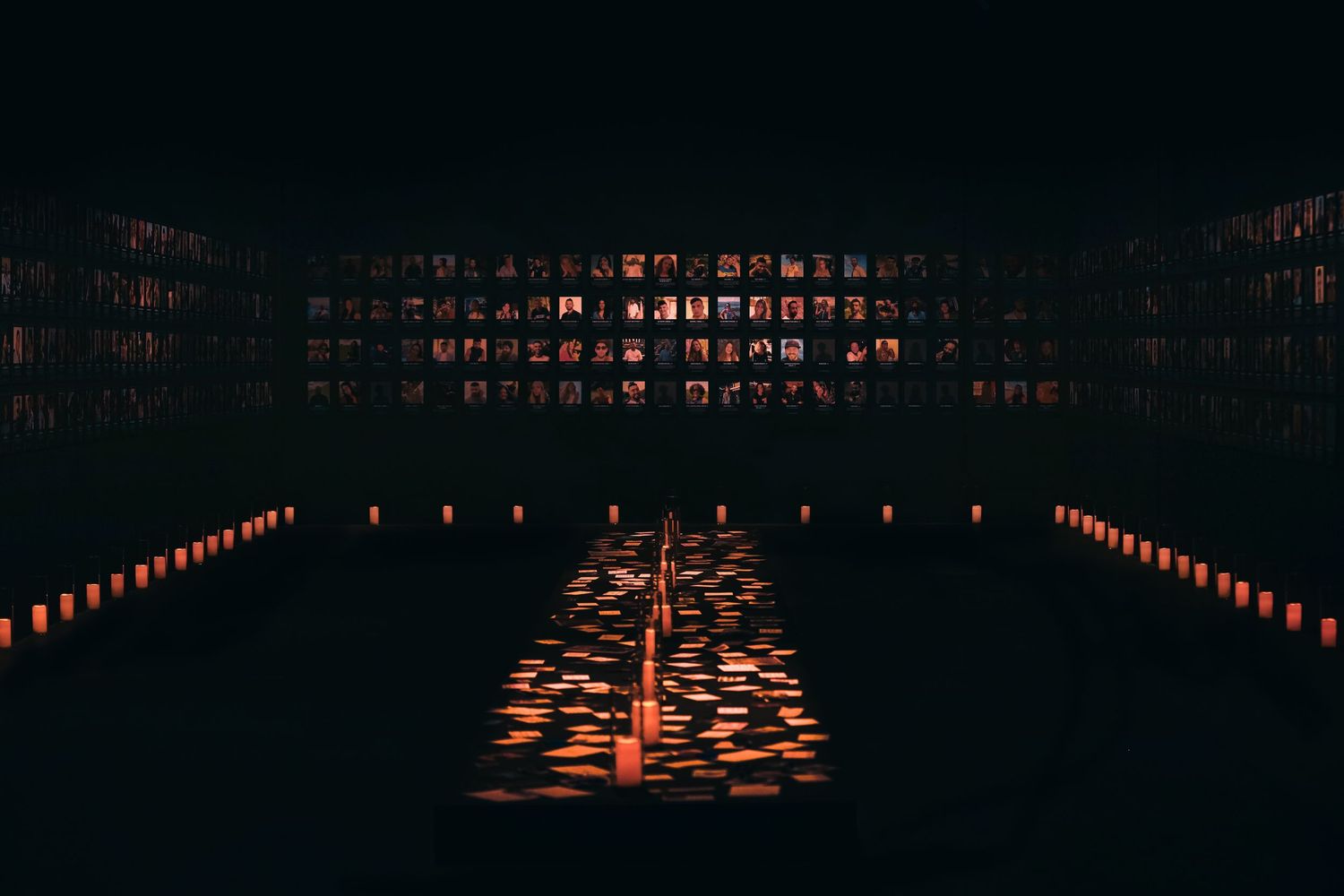 Dark room illuminated by rows of glowing candles reflecting on floor.